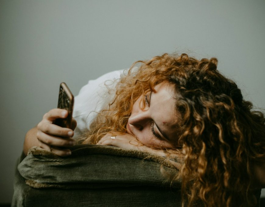 Woman with dating app burnout lying down while holding her phone
